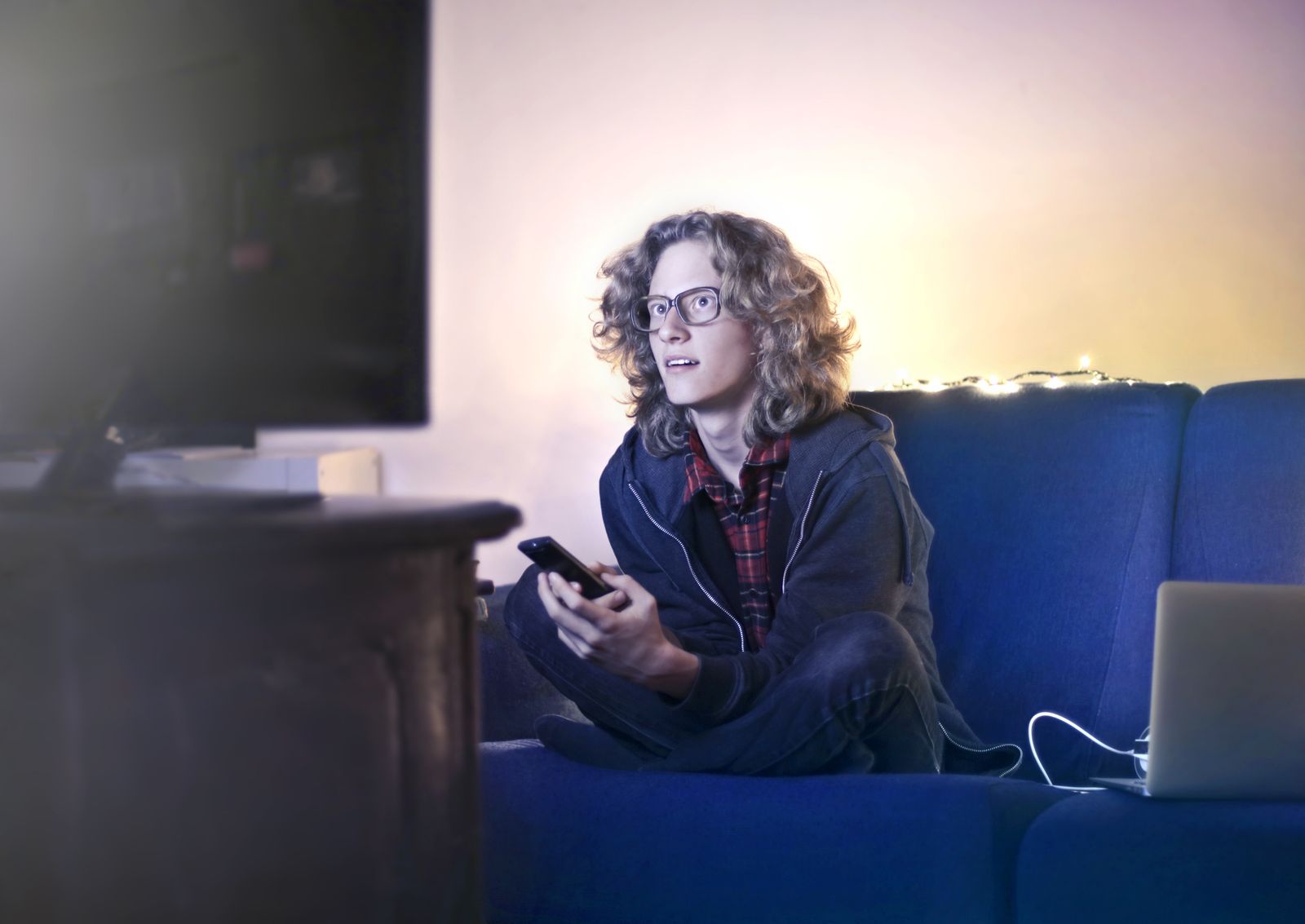 Man on a couch watching TV with his phone